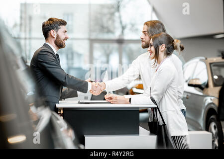 Young business giovane agitando mani avente una trattativa con l'addetto alle vendite presso lo stand di acquisto o noleggio di auto nello showroom Foto Stock
