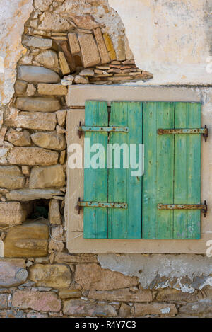 Una vecchia e abbandonata la parete con un dipinto di verde shabby chic stile sportello di legno. Finestra rustico con peeling vernice sulle tradizionali persiane in legno. Foto Stock