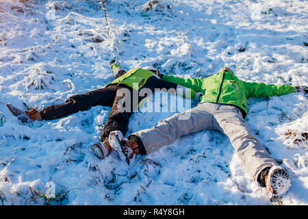 Coppia giovane in amore giacente in presenza di neve e di rendere gli angeli di neve. Le persone felici al divertimento in inverno foresta. Attività stagionali Foto Stock