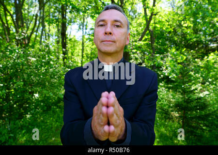 Guardare un buon sacerdote cattolico prega con noi nella gioia. Egli guarda a noi con fiducia, apertura di braccia in pace. Focus sul viso. Foto Stock