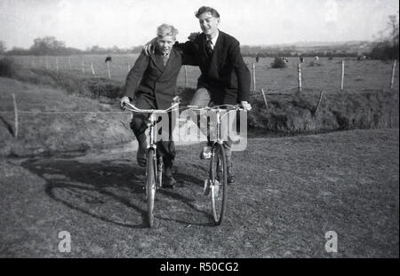 Degli anni Cinquanta, storico, due ben vestito giovani uomini seduti sulle loro biciclette accanto a ogni altra fuori su un orlo erbosa in campagna, England Regno Unito. Foto Stock