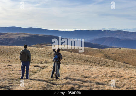 Due escursionisti con zaini guardando ai vasti altopiani e lontani gli strati di montagna sopra le nuvole Foto Stock