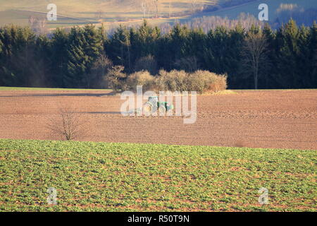 Il trattore lavora in azienda, un moderno trasporto agricolo, un agricoltore lavora nel campo, terra fertile, il trattore su sfondo al tramonto, coltivazione o Foto Stock