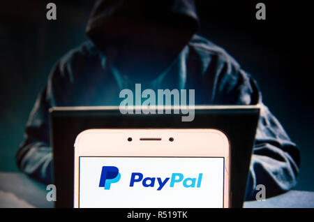 American online piattaforma di pagamento Paypal logo è visibile su un androide dispositivo mobile con una figura di hacker in background. Foto Stock