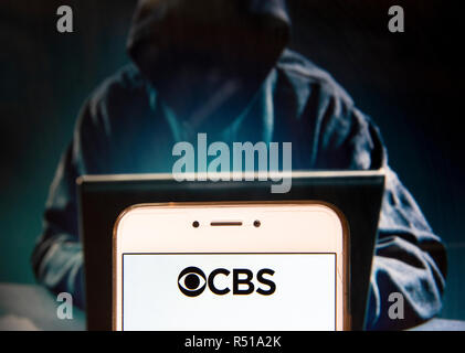 Inglese americano della lingua di diffusione commerciale di rete della radio e della televisione CBS logo è visibile su un androide dispositivo mobile con una figura di hacker in background. Foto Stock