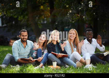 Mixed-gara gruppo di studenti seduti insieme sul prato verde del campus universitario Foto Stock