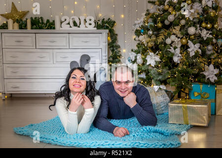 Coppia giovane in amore su un plaid blu sullo sfondo di un albero di Natale decorato Foto Stock