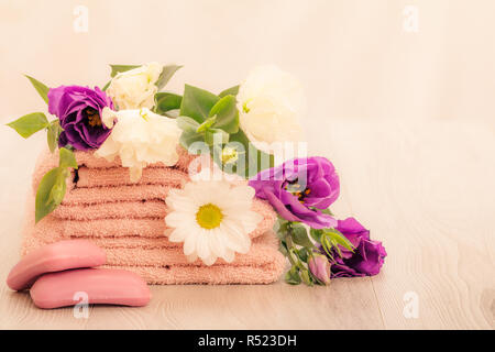 Pila di soffici asciugamani di spugna con bianco e fiori viola, sapone su sfondo rosa. I prodotti spa. Foto Stock