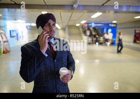 Giovane bello indiano imprenditore Sikh alla stazione metropolitana parlando al telefono Foto Stock