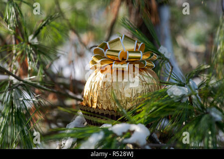 Vacanze inverno concetto di decorazione: Italiano sfera di cioccolato avvolto in oro metallizzato in lamina e rabboccato con la golden nastri, fiocchi e congelata coperta di neve p Foto Stock