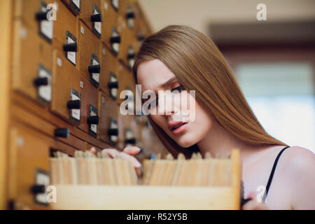 Bella ragazza giovane con capelli neri dritti apre la casella e la ricerca dei dati nel file cabinet nella libreria Foto Stock