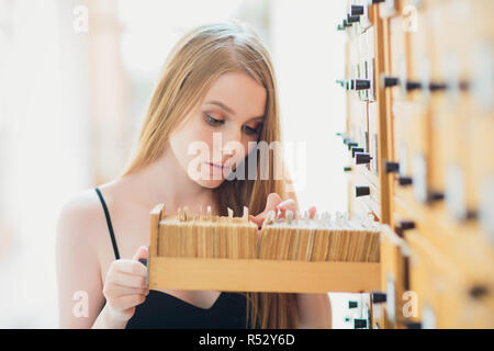 Bella ragazza giovane con capelli neri dritti apre la casella e la ricerca dei dati nel file cabinet nella libreria Foto Stock