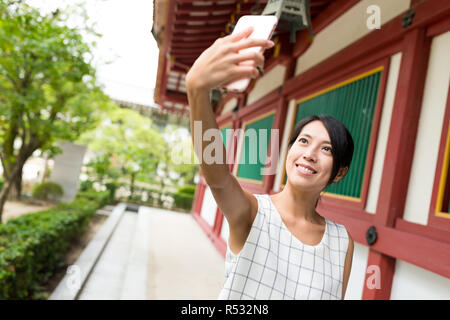 Donna prendendo selfie dal telefono mobile nel tempio giapponese Foto Stock