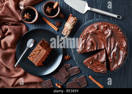 In casa la torta al cioccolato a strati con confettura di albicocca e guarnita con glassa al cioccolato servito su una piastra nera con vin brulé in tazze di terracotta accanto Foto Stock