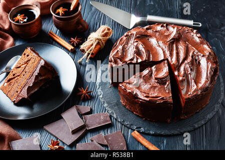 Close-up di cioccolato artigianale torta decorata con glassa al cioccolato servito su una piastra nera con vin brulé in argilla tazze rustico accanto a un nero wo Foto Stock