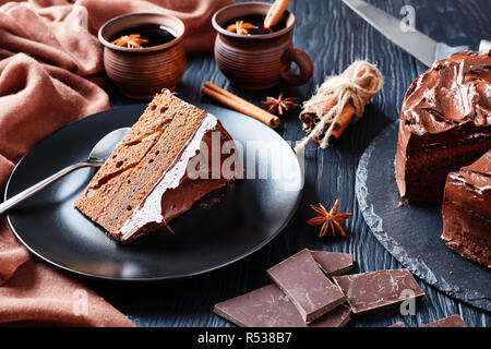 Porzione di torta al cioccolato con marmellata di albicocche il riempimento e rabboccato con glassa al cioccolato servito su una piastra nera con vin brulé in argilla tazze rustico su un bla Foto Stock
