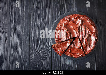 Fette di torta al cioccolato con marmellata di albicocche il riempimento e rabboccato con glassa al cioccolato su una lastra di pietra su tavoli in legno nero, vista orizzontale dal di sopra, fl Foto Stock
