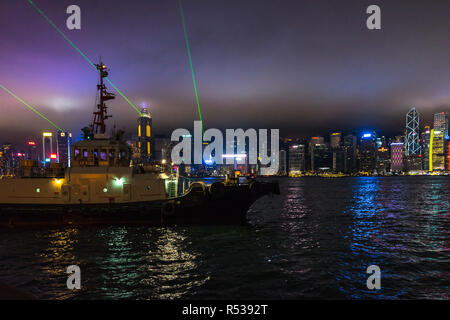 Una barca da pesca vela il Victoria Harbour con Hong Kong Central grattacieli sullo sfondo durante la Sinfonia di Luci show. Foto Stock