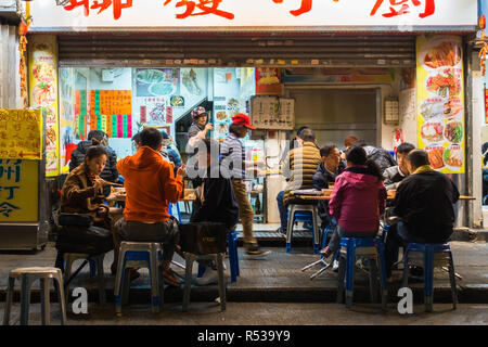 Scena di strada con persone locali cenare presso un venditore ambulante di Mong Kok area. Di Hong Kong, Kowloon, Gennaio 2018 Foto Stock