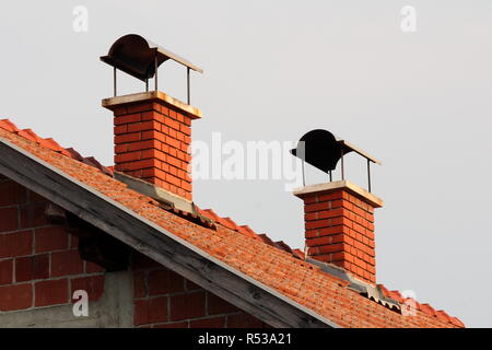 Rosso mattone camini con protezione metallica sulla parte superiore su incompiuta suburban casa familiare con cielo chiaro in background Foto Stock