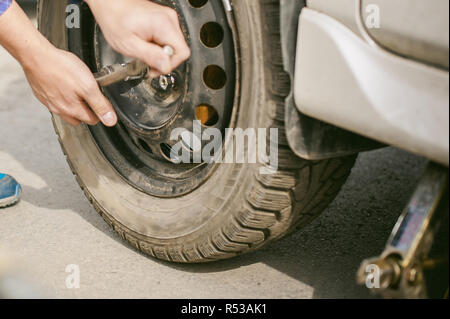 L'uomo la sostituzione di una ruota sulla strada. sul modo in cui vi è stata la rottura della ruota, forare necessarie per sollevare il cric e rimuovere la ruota allentando i dadi. problemi su strada di viaggiatori. Fai da te Foto Stock