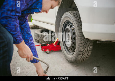 L'uomo la sostituzione di una ruota sulla strada. sul modo in cui vi è stata la rottura della ruota, forare necessarie per sollevare il cric e rimuovere la ruota allentando i dadi. problemi su strada di viaggiatori. Fai da te Foto Stock