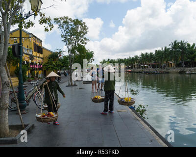 Due donne Vietnameses stanghe chiamato anche un polo di spallamento o un milkmaid il giogo di bambù sul lungomare della città Antica di Hoi An Vietnam Asia entrambi Foto Stock