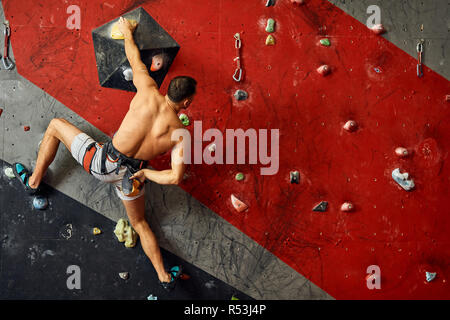 Panoramica del giovane uomo muscolare in allenamento indoor clymbing palestra. Foto Stock