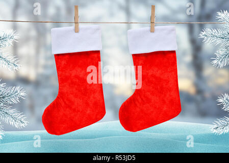 Natale calzini rossi agganciato con un clip su una fune. In inverno, la scena di neve con albero di Natale in background. Foto Stock
