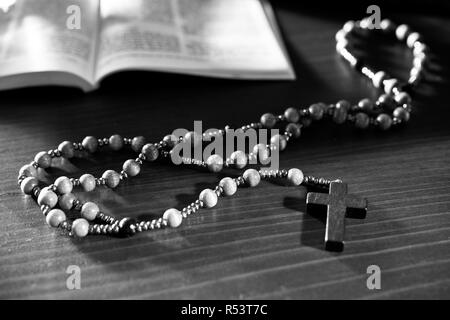 Rosario e la bibbia sul tavolo di legno. In bianco e nero. Foto Stock