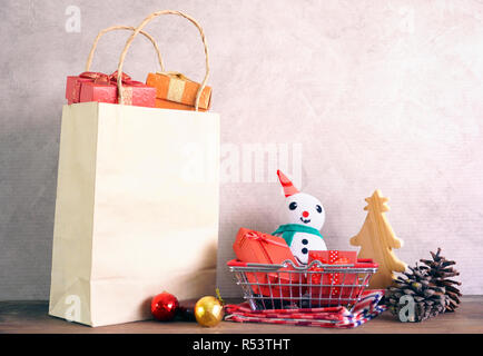 Confezioni regalo in busket e dono nel sacchetto di carta e uomo di neve e albero di Natale rendono da legno sulla tavola di legno Foto Stock