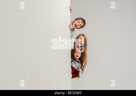 Banner con sorpresa di vedere i bambini sbirciare il bordo con copyspace. Il ritratto del piccolo grazioso ragazzo di ragazzi e ragazze guardando la telecamera contro studio bianco parete. Moda per bambini e felice concetto emozioni Foto Stock