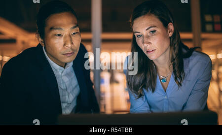 Partner commerciali multietnici che lavorano fino a tarda notte in ufficio. colleghi d'affari seduti insieme a guardare un notebook che lavora a tarda notte Foto Stock