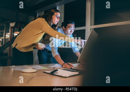 donna d'affari che mostra qualcosa sullo schermo del computer al suo socio d'affari. uomo d'affari e donna che lavorano insieme a tarda notte in ufficio. Foto Stock