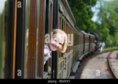 Passeggero ragazza di giovani di età compresa tra i 8 / 8 anni, sorridente e guardando fuori della finestra di un movimento del treno di trasporto sulla isola di Wight linea ferroviaria a vapore. Regno Unito. (98) Foto Stock