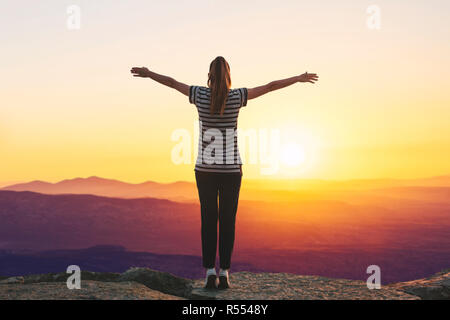 Una ragazza si erge sulla cima di una montagna in solitudine, si ammira la splendida vista del paesaggio naturale e solleva le mani in alto mostra come essa è libera e felice. Foto Stock