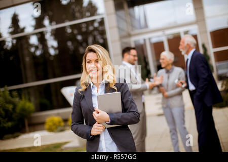 Giovani busenesswoman outdoor permanente e tenendo un documenti mentre altri business persone che parlano in background Foto Stock