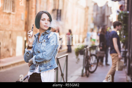 Ritratto di una giovane donna di fumare una sigaretta elettronica in strada Foto Stock