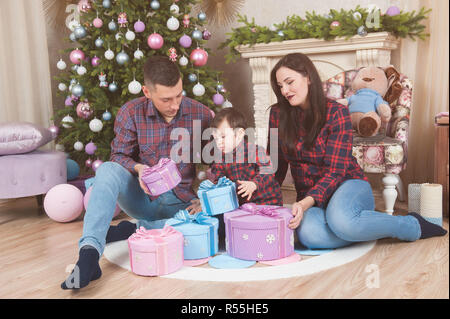 Felice giovani caucasici famiglia padre madre e bambino piccolo con scatole di regali di Natale nelle decorazioni di Natale Foto Stock