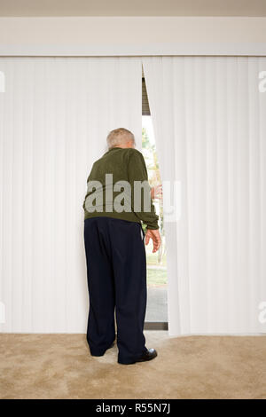 Uomo anziano guardando fuori di persiane Foto Stock