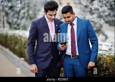 Due eleganti indiano mans alla moda modello sulla tuta poste al giorno d'inverno guardando al telefono. Foto Stock