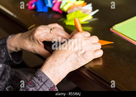 Le mani di lady senior di piegatura della carta origami Foto Stock