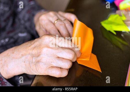 Le mani di lady senior di piegatura della carta origami Foto Stock