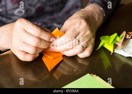 Le mani di lady senior di piegatura della carta origami Foto Stock