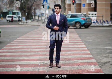 Elegante indiano uomo macho modello sulla tuta e cravatta rosa a piedi a croce pedonale. Foto Stock