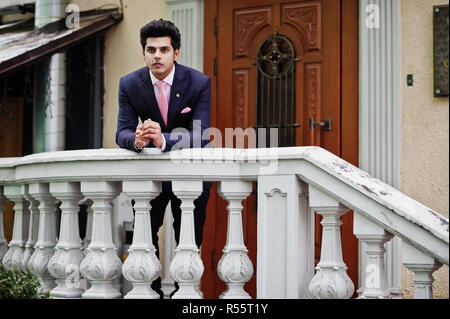 Elegante indiano uomo macho modello sulla tuta e cravatta rosa appoggiato su di una ringhiera. Foto Stock