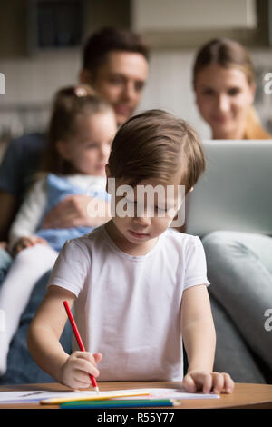 Little Boy disegno mentre i genitori a giocare con la figlia Foto Stock