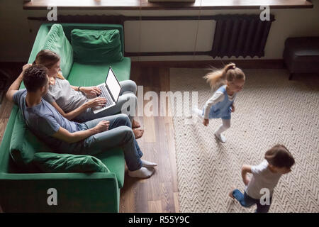 I bambini giocando catch-up mentre i genitori usando il computer portatile Foto Stock