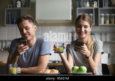 Felice coppia giovane utilizzando gli smartphone durante la prima colazione Foto Stock