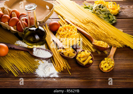 Non cotti gli spaghetti e la pasta su un tavolo con le uova e la farina e olio di oliva Foto Stock